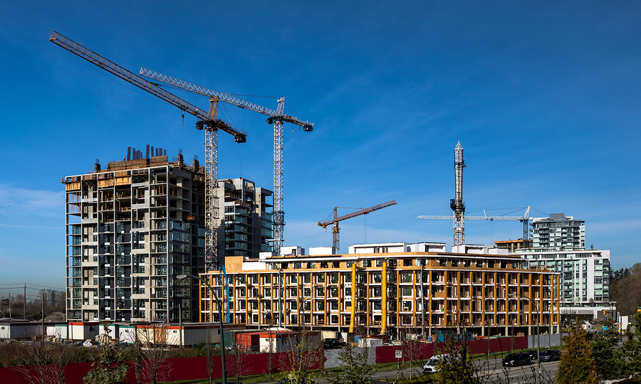 Wide view of multifamily residential construction sites in a city with multiple cranes against a blue sky