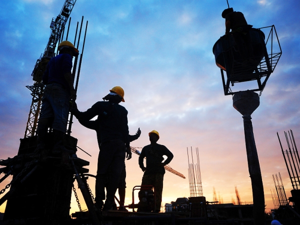 Construction workers on a building site silhouetted by a sunrise