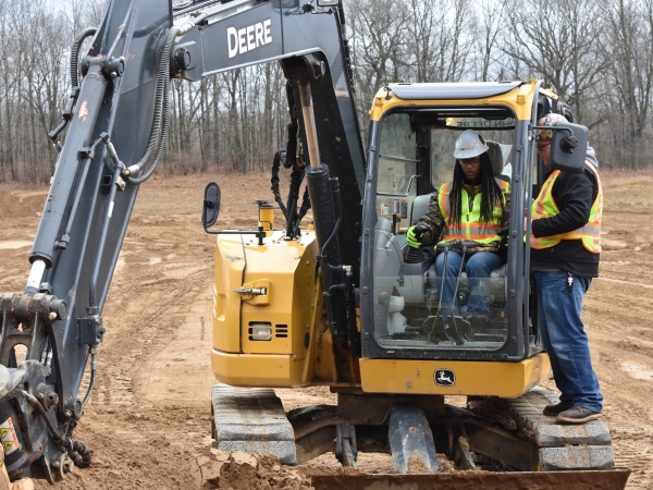 Operator instructs another operator on the controls of a backhoe