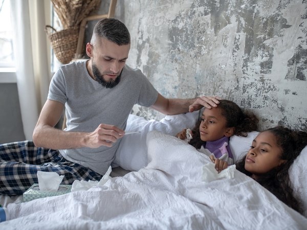 Father checks sick daughters' temperature in bed