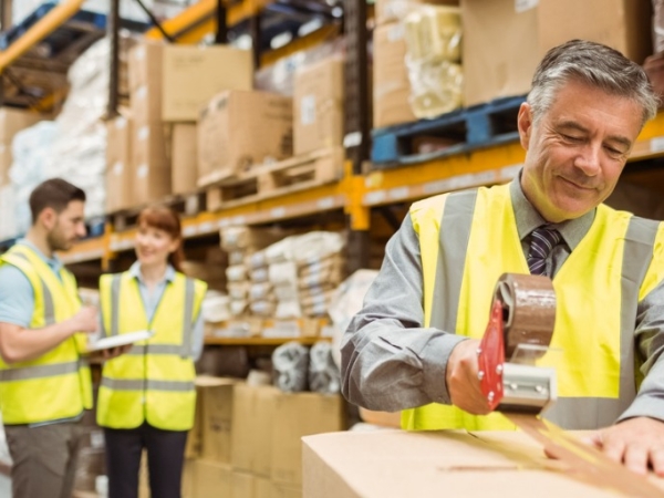 Older man in high-viz vest contentedly packing boxes in a warehouse