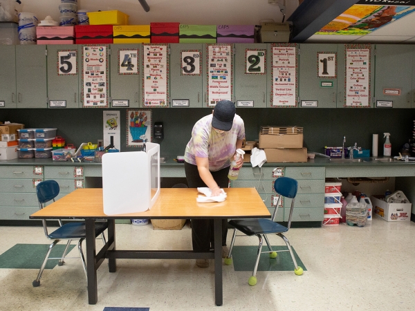 Elementary school custodian wipes table in classroom