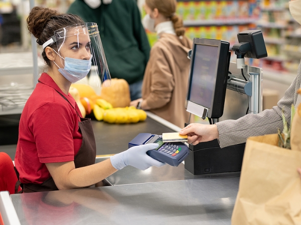 Cashier in COVID protective gear accepts payment