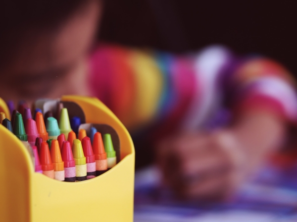 Child at day-care center colors with crayons, crayons in foreground in focus