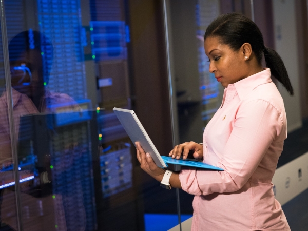 Businesswoman in pink suit checks laptop in server room
