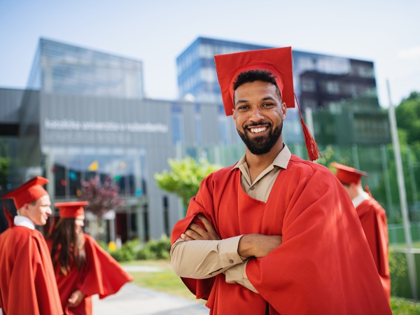 Graduate in cap and gown faces camera with modern buildings in background