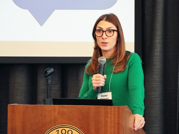 Alyssa Stewart at lectern in front of screen, with microphone and green shirt