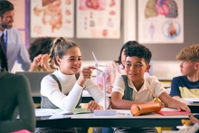 Students in a classroom examine a wind turbine model with guarded enthusiasm